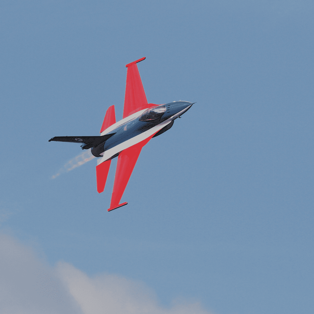 A navy blue and red fighter jet soars through a clear sky, leaving a faint white trail behind.