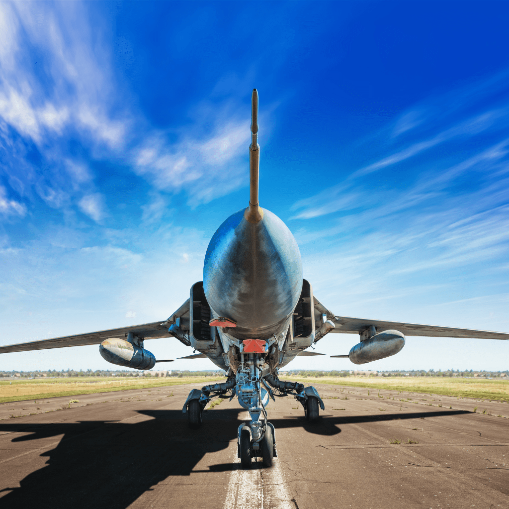 A close-up view from the front of a military jet aircraft on a runway with a clear blue sky in the background.